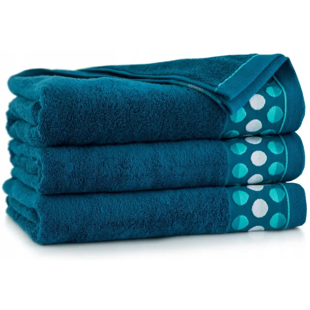 Zwoltex håndklær Zen2, tre mørkeblå bomullshåndklær med turkise kanter og hvite prikker, sett fra siden.