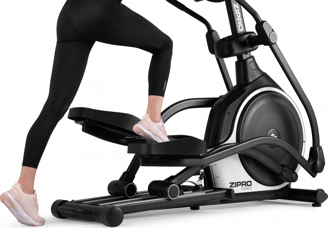 Orbitrek svart og hvit ellipsemaskin i bruk, sett fra siden av person med svarte tights og lyse joggesko.