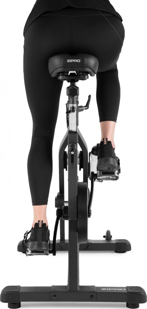 Spinnsykkel i sort metall sett bakfra, person med svarte tights sykler, ZIPRO-logo synlig på setet.