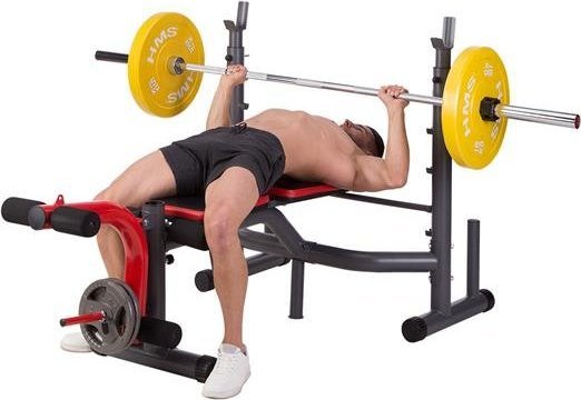 Multifunksjonell Treningsbenk med rød og svart polstring, person løfter vektstang med gule vektskiver fra siden.