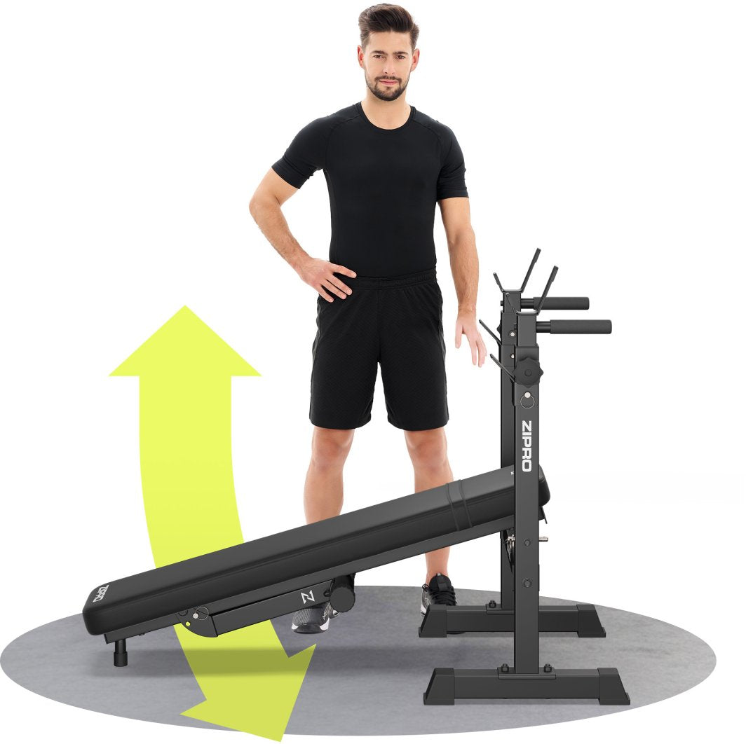 Treningsbenk Sammenleggbar i sort metall med justerbar vinkel, mann i sort tøy ved siden av, gul pil viser retning.