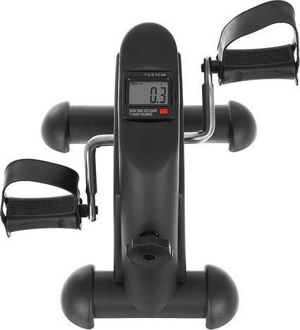 Treningssykkel i sort med to pedaler, justerbare stropper og LCD-skjerm, sett ovenfra på robust base.