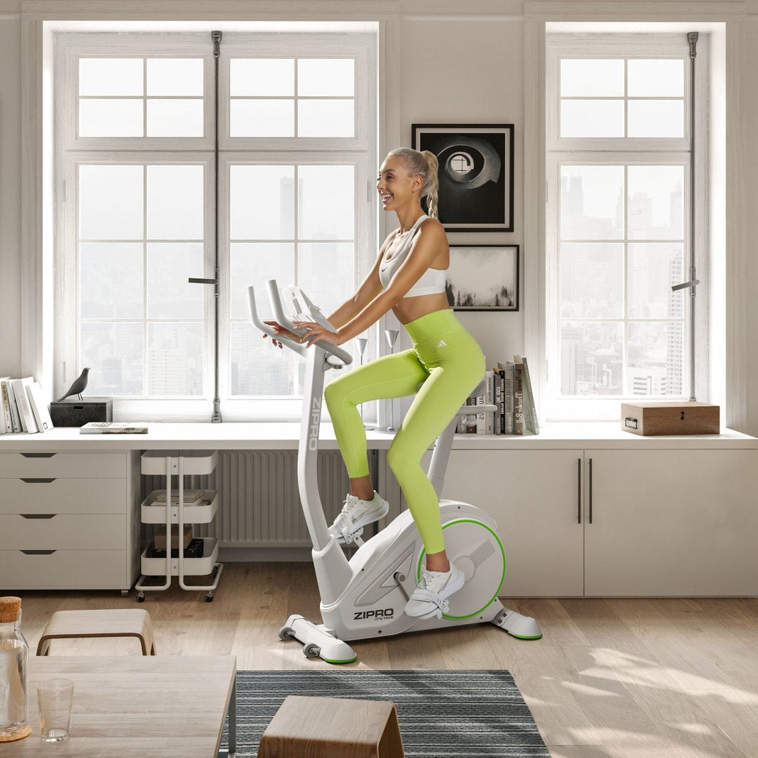 Trimsykkel i hvit og grå med grønne detaljer brukes av kvinne i treningsklær i lyst, moderne rom.