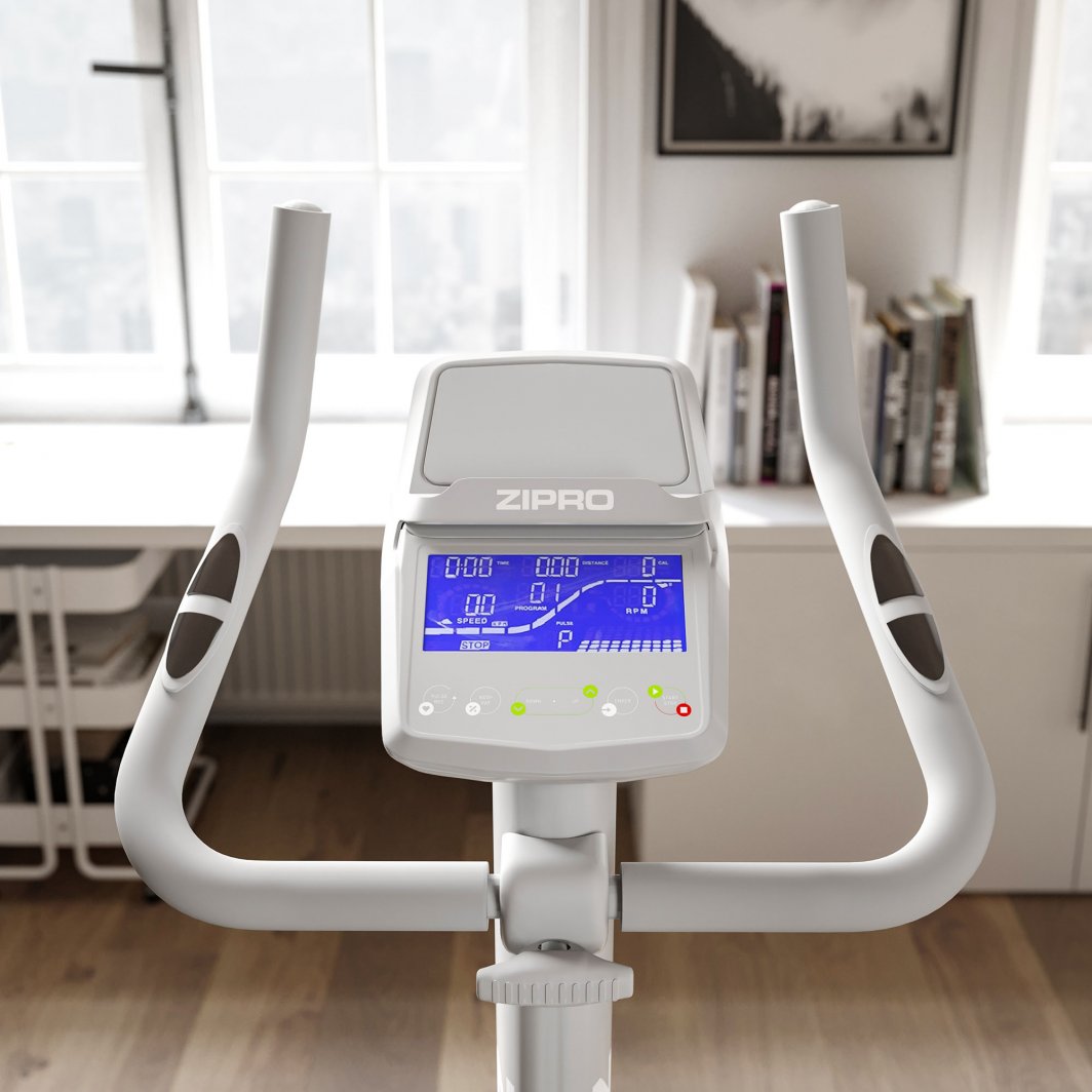 Treningssykkel med grå og svarte håndtak, elektronisk display, fotografert forfra i lyst rom med vindu og bokhylle.