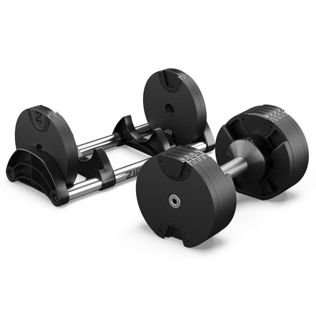 Justerbara Hantlar i svart metall og plast, sett skrått forfra, med stativ og ekstra vektskiver bak.
