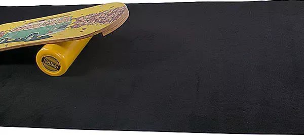 Tykk Treningsmatte i svart, sett skrått ovenfra, med hjørnet av skateboard med gule hjul øverst til venstre.