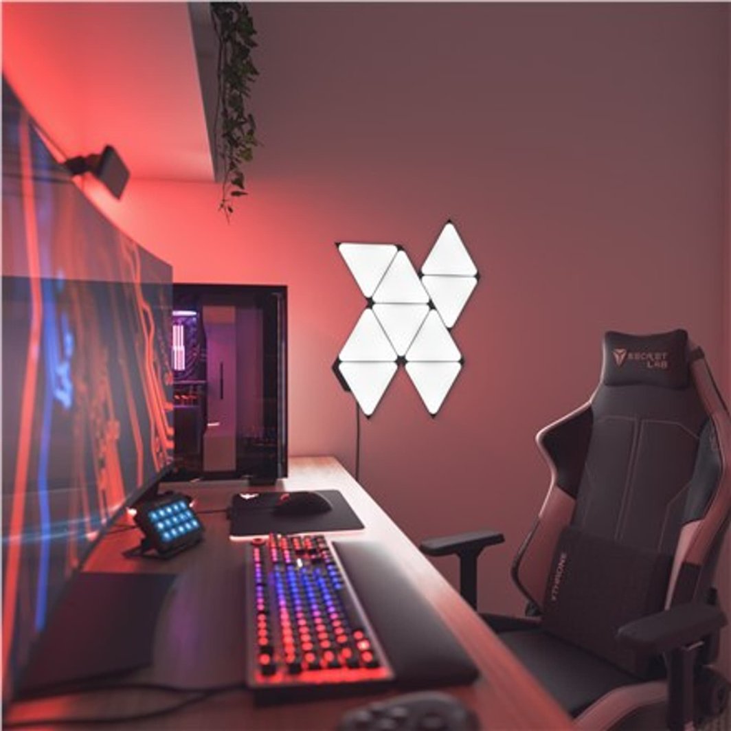 Tredemølle lyspaneler smarte trekanter fra Nanoleaf montert på vegg i moderne gaming-oppsett.