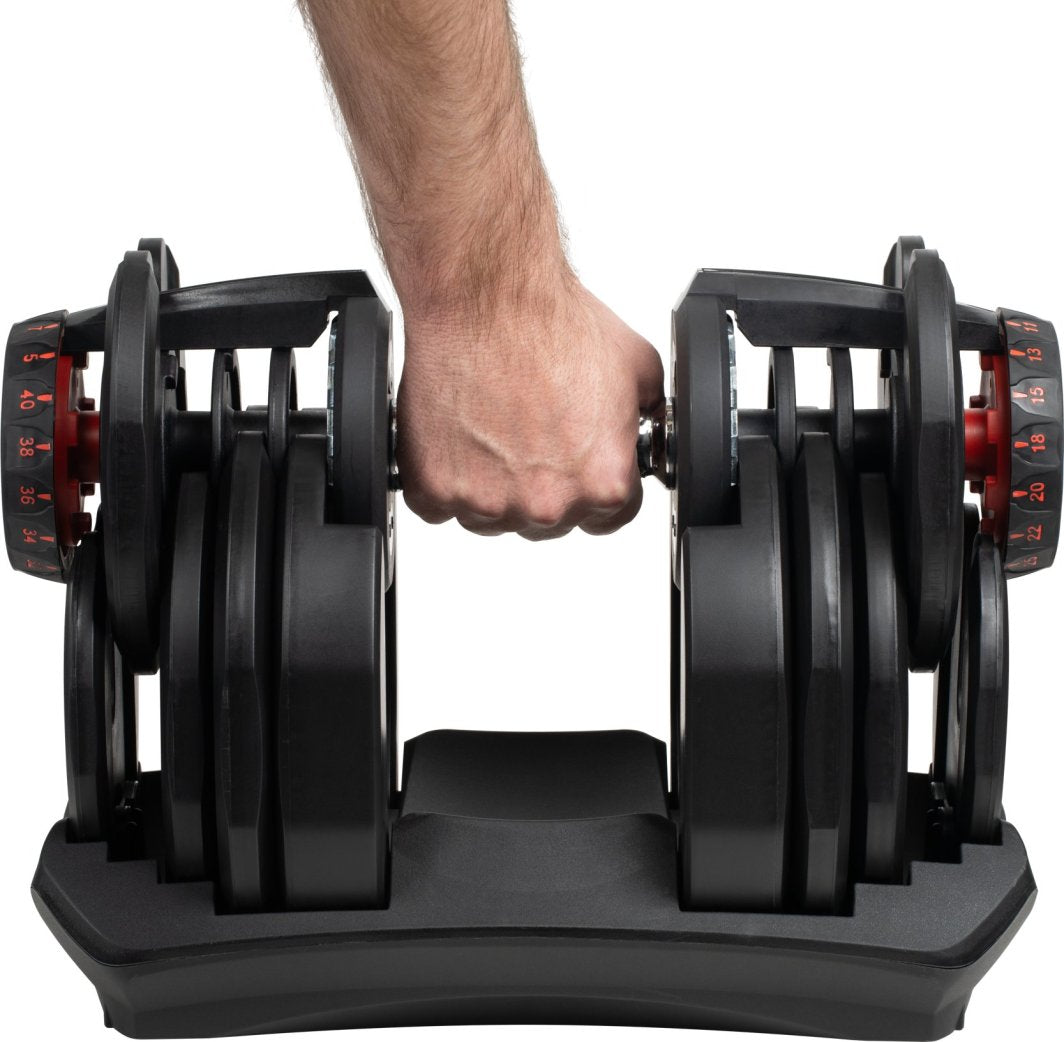 Manual Manual justerbar i sort plast og metall, hånd griper håndtak, synlige vektskiver og rød justeringsmekanisme.