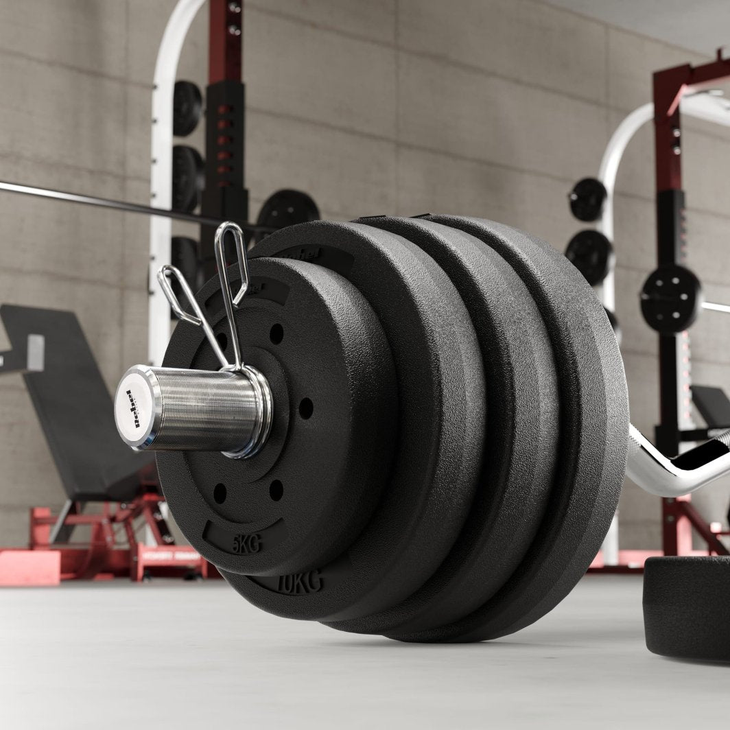 Vektskiver i sort metall på vektstang med fjærlås, fotografert fra siden i lyst treningsrom.