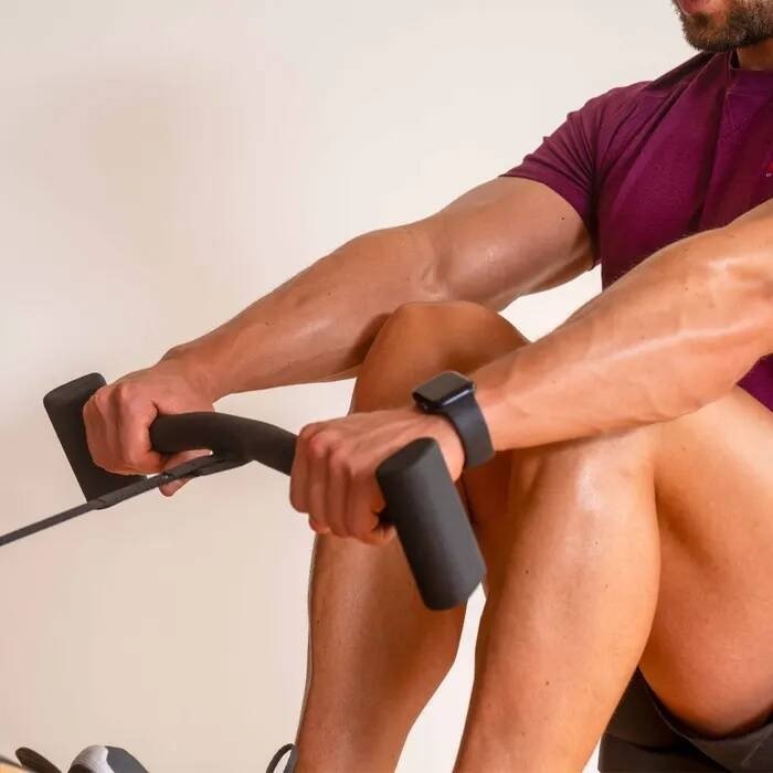 Romaskin Trening med mann i treningstøy som holder svarte, polstrede håndtak på romaskinen, nærbilde fra siden.