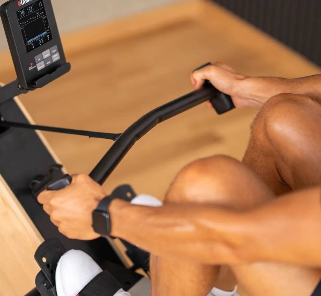 Romaskin Sammenleggbar med sort metallramme, digital skjerm og håndtak, person i bruk, nærbilde av armer og ben.