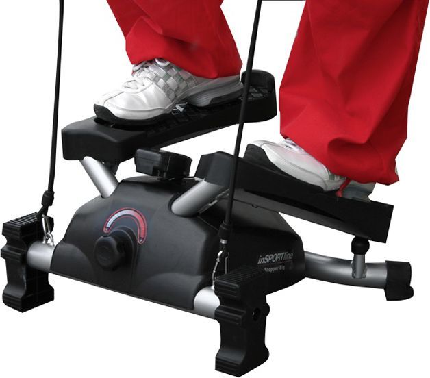 Stepmaskin i sort og sølv med to fotplater, strikkhåndtak og person med røde bukser og hvite sko, sett fra siden.