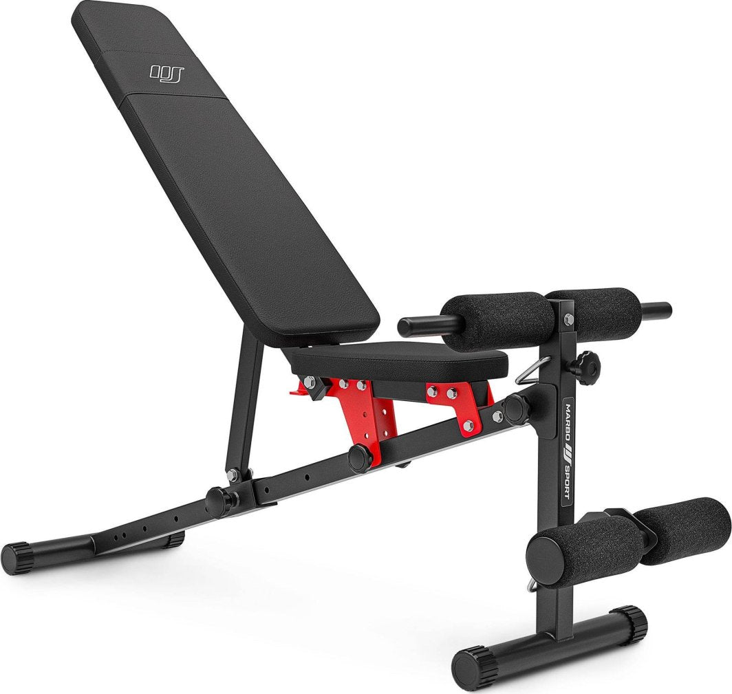 Treningsbenk i svart og rødt stål med polstret sete og rygg, skumruller for bein, avbildet fra siden.