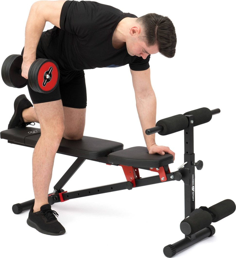 Treningsbenk med svarte og røde detaljer sett fra siden, person trener med manual, polstrede puter synlige.