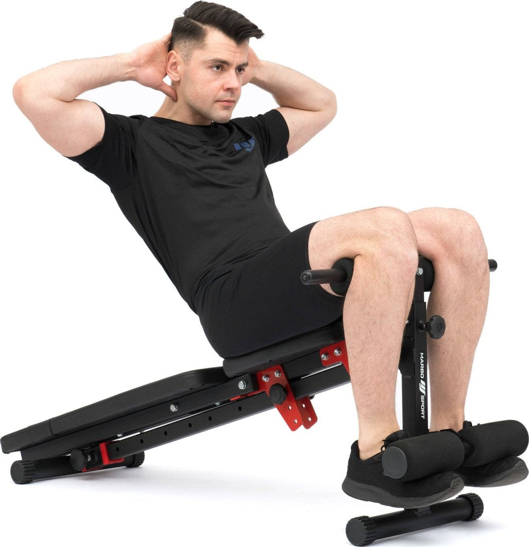 Multifunksjonell Treningsbenk i svart og rødt, med polstrede puter. Person gjør situps fra siden på benken.