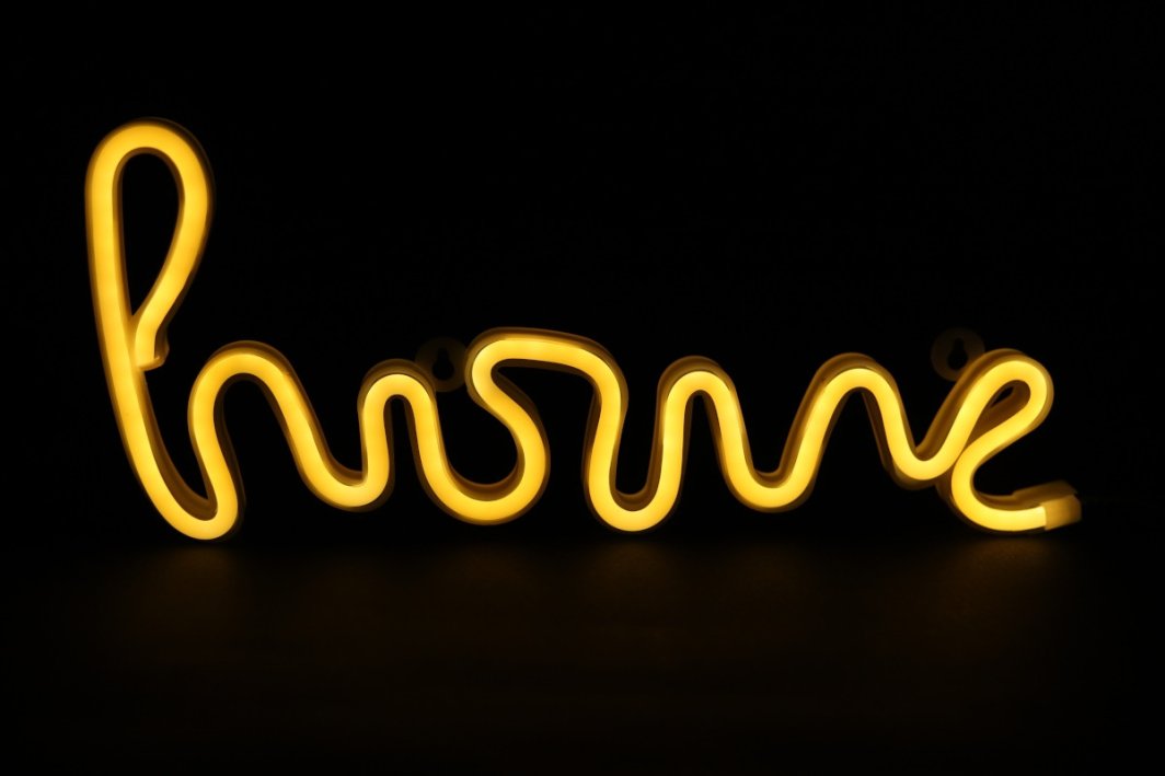 Tredemølle neonskilt HOME i gul LED med varm glød, håndskriftstil, sett forfra mot svart bakgrunn.
