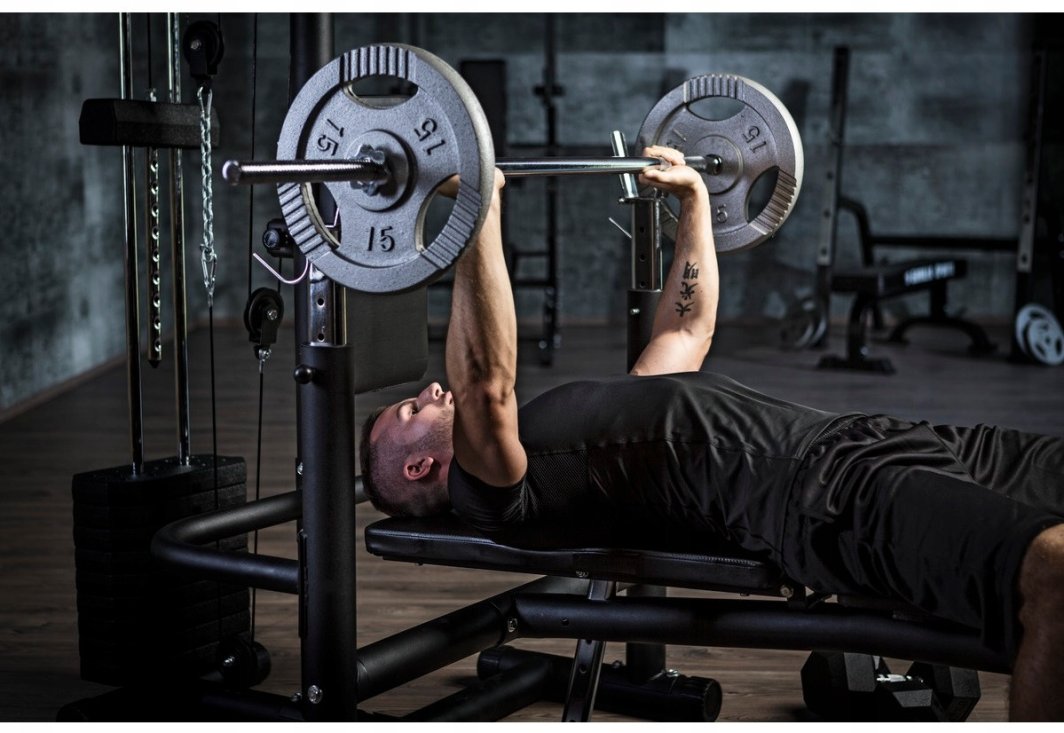 Vektskive 15kg vinyl med 30mm hull brukes på vektstang under benkpress i treningsstudio, sett fra siden.
