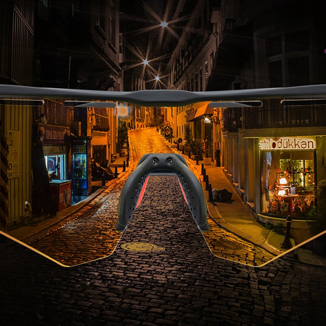 Sportsbriller med gult glass og sort nesebro, utsyn mot opplyst gate om kvelden, viser synsfelt og kontrast.