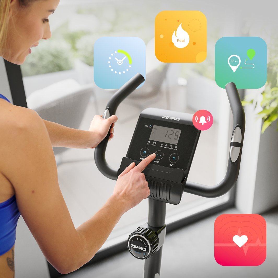 Treningssykkel med sort styre og digitalt display, en person i treningstøy bruker kontrollpanelet.