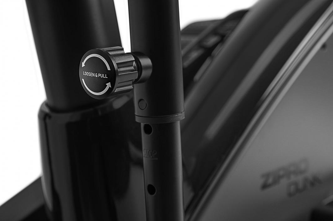 Ellipsemaskin justeringsskrue i sort metall med teksten "LOOSEN & PULL" på rammen, sett fra siden.