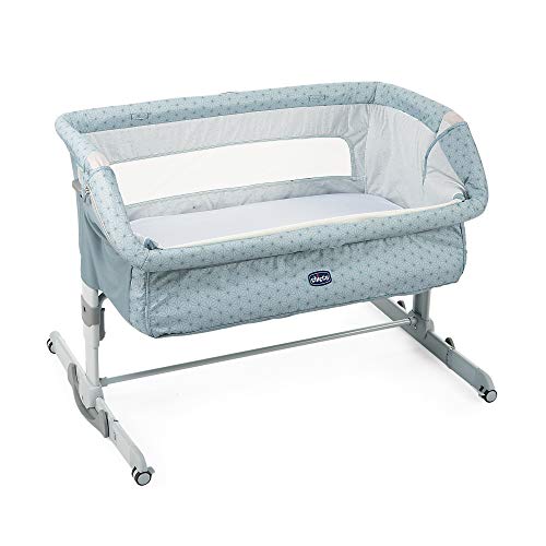 Bedside Crib i lyseblått stoff med mønster, metallben, hvite plastdetaljer og nettinglomme på siden.