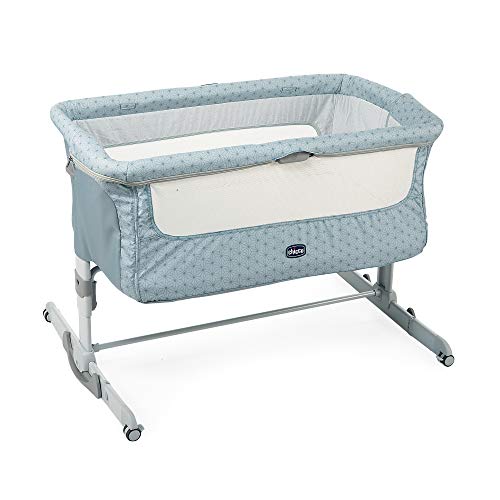 Crib i lyseblått stoff med små mønster, nettingpanel på siden og justerbare ben med hjul, sett skrått forfra.