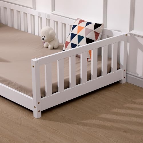 Juniorseng i hvitmalt furu med beige madrass, fargerik pute med mønster og hvit kosebamse, sett fra siden.