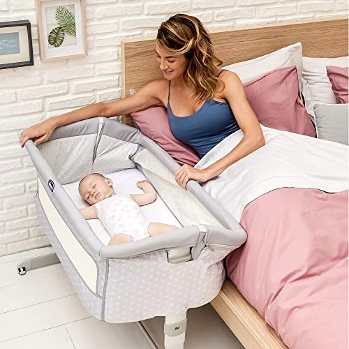 Babyseng med grå kanter og hvitt mønster, baby sover ved siden av voksen seng, kvinne ser på barnet.