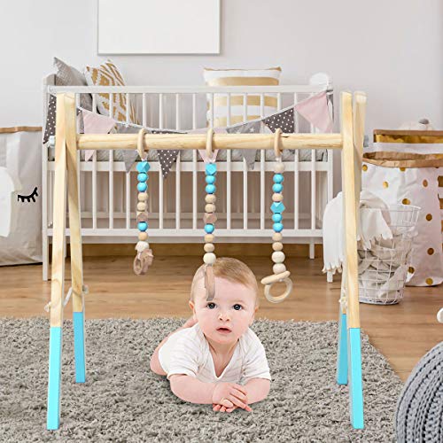 Babygym i lyst tre med blå detaljer, treleker og ringer henger over en baby som ligger under stativet.