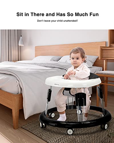 Gåstol i sort og hvit plast med seks hjul, barn sitter i stolen og holder i bordet, soverom i bakgrunnen.