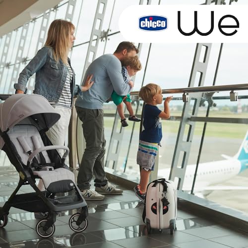 Trillevogn i grå og svart sett fra siden i lyst rom, familie og liten koffert i bakgrunnen.