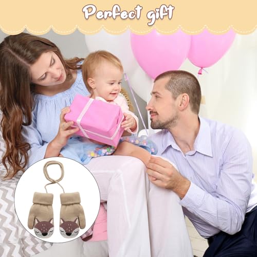 Votter Baby beige med dyremotiv og snor vises foran en familie med barn, ballonger og gaveeske i bakgrunnen.