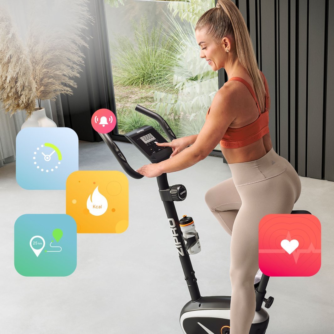Treningssykkel i svart og grått med digital skjerm, vannflaskeholder og kvinne i treningstøy som trener.