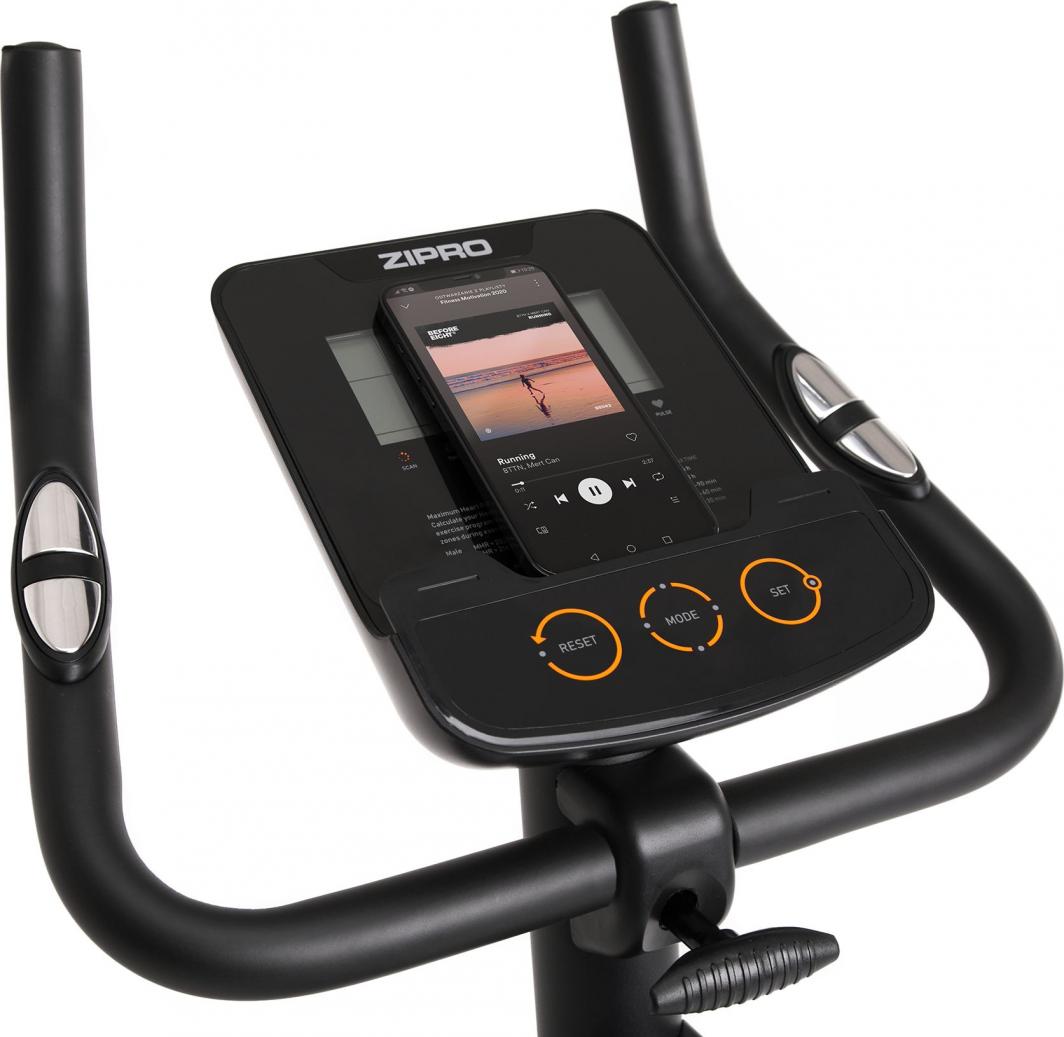 Ergometersykkel med digitalt display, funksjonsknapper, pulssensorer og mobiltelefon plassert på skjermen.