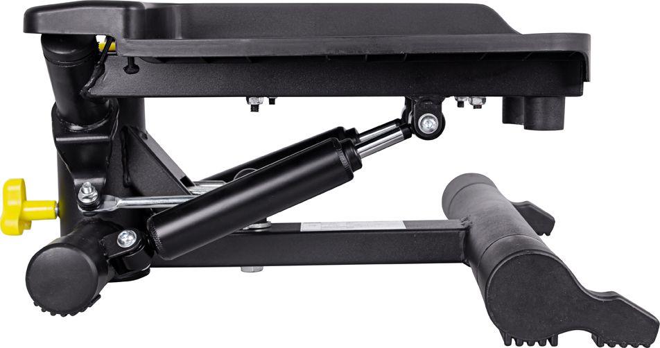 Stepper Trening sort mekanisk stepmaskin med gule knotter, sylinder og rillede fotplater, sett fra siden.