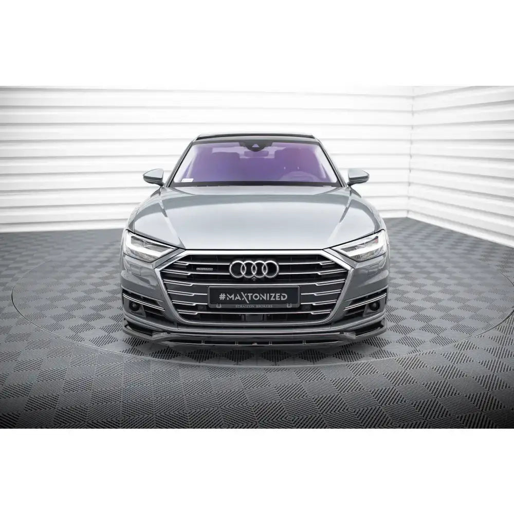 Front lip på Audi A8 D5, grå bil forfra med kromgrill og lilla frontrute i lyst rom.