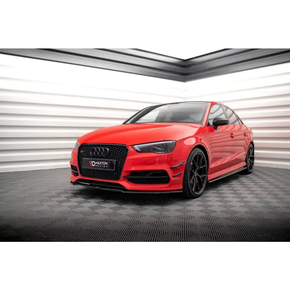 Frontspoiler på rød Audi S3 med svarte felger, sett skrått forfra innendørs mot lys vegg.