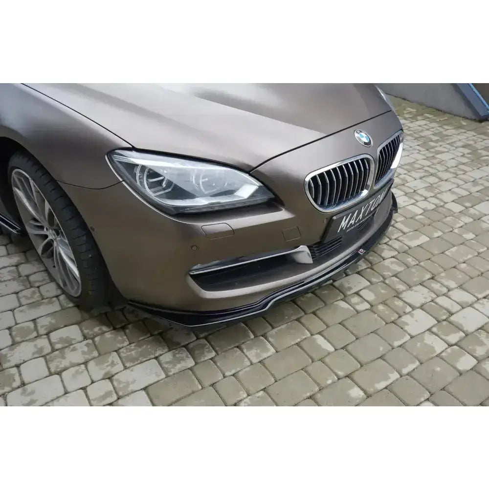 Front lip på BMW 6 Gran Coupé, nærbilde av sort leppe, frontfanger og detaljer mot steinbelagt underlag.