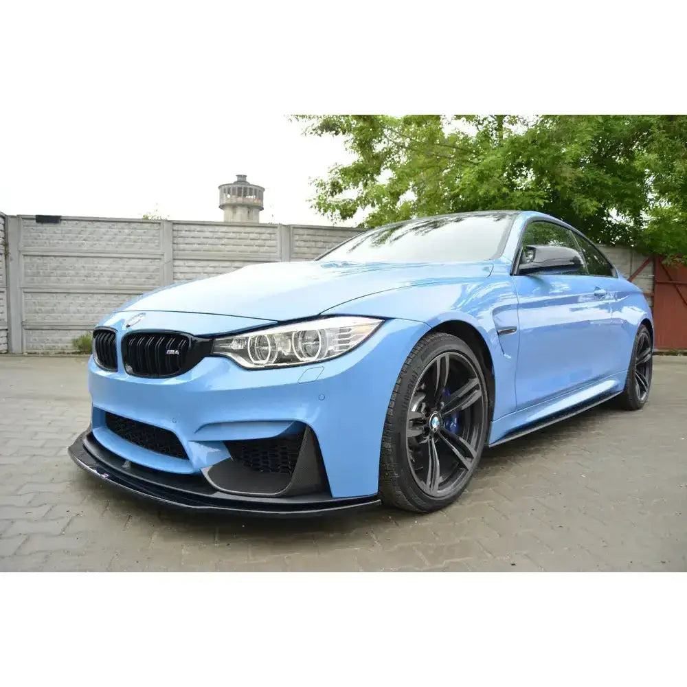 Front lip på BMW M4 F82 M-Performance med sorte detaljer, sett skrått forfra på asfalt foran gjerde.