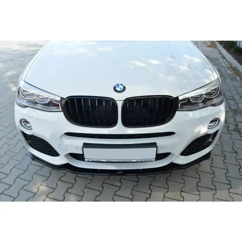 Frontsplitter på BMW X4 M-Pack, sort spoiler foran hvit bil med svarte nyregriller og frontlykter.