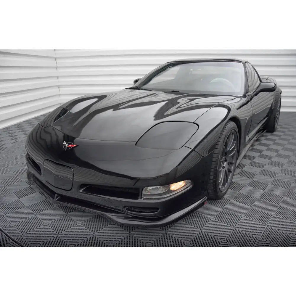 Frontspoiler på svart Chevrolet Corvette C5 med blank lakk og mørke felger, innendørs på mønstret gulv.