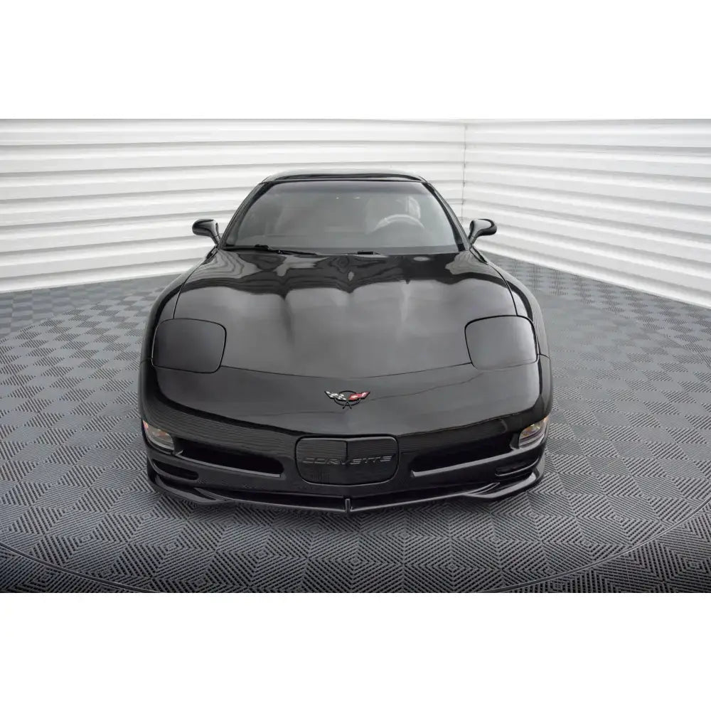 Frontsplitter på sort Chevrolet Corvette C5 sett forfra med logo, lysgrå vegger og rutete gulv.