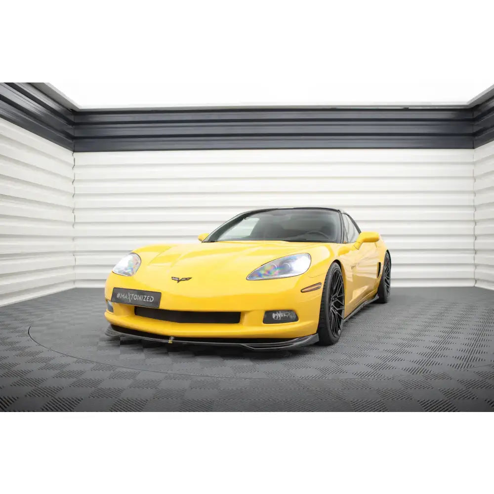 Frontspoiler på gul Chevrolet Corvette C6 med svarte felger, sett forfra i lyst rom med grått gulv.