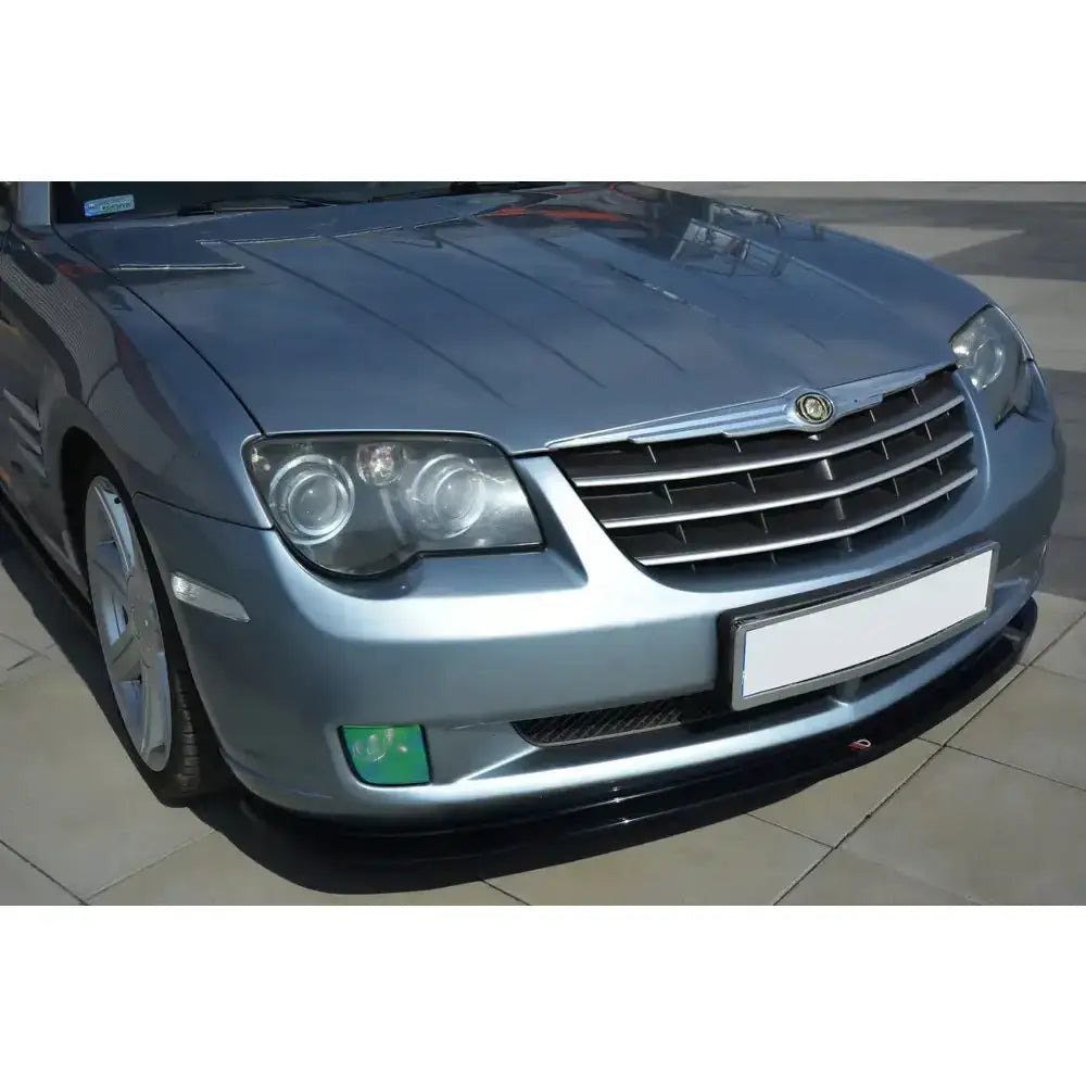 Frontleppe på Chrysler Crossfire i metallisk blå med grå grill og runde hovedlykter, sett fra skrå vinkel.