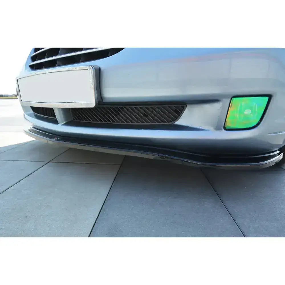 Frontsplitter på Chrysler Crossfire med svart spoiler, grønnaktig tåkelys og synlig grill parkert på fliser.