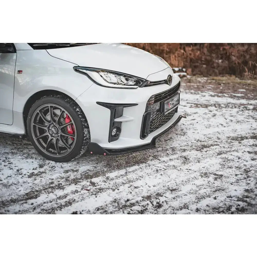 Front splitter på hvit Toyota GR Yaris Mk4 med sorte felger, røde bremsekalipere og snødekket bakke.