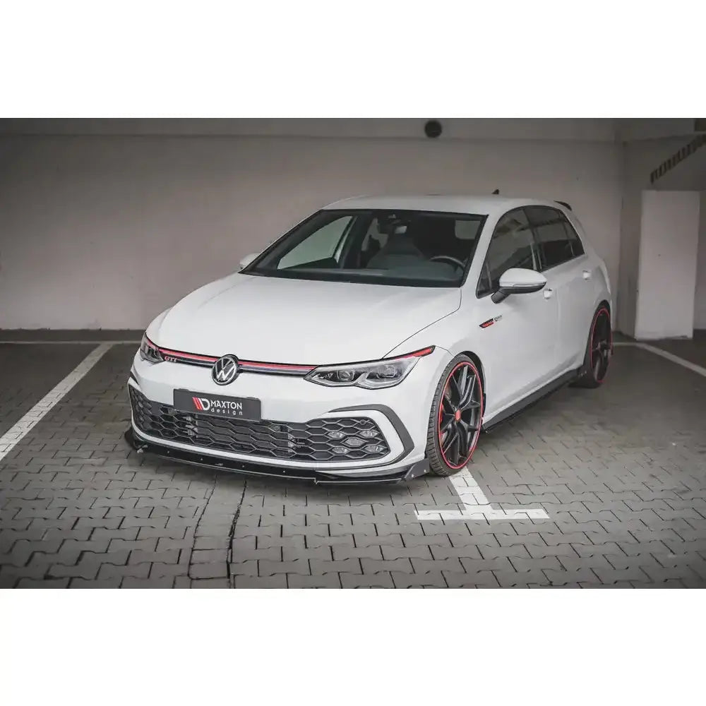 Frontspoiler på Volkswagen Golf 8 GTI med sorte felger og røde detaljer, fotografert i parkeringshus.