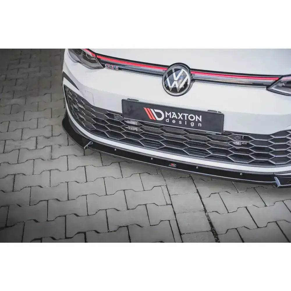 Front lip på Volkswagen Golf 8 GTI med sort frontsplitter, heksagonalt grillmønster og røde detaljer.