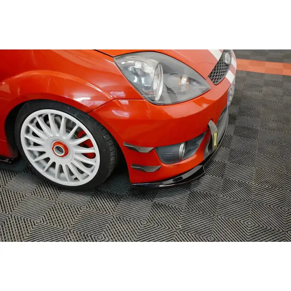 Front lip på rød Ford Fiesta VI ST med hvite felger, synlig frontlykt og sorte aksenter, sett skrått forfra.