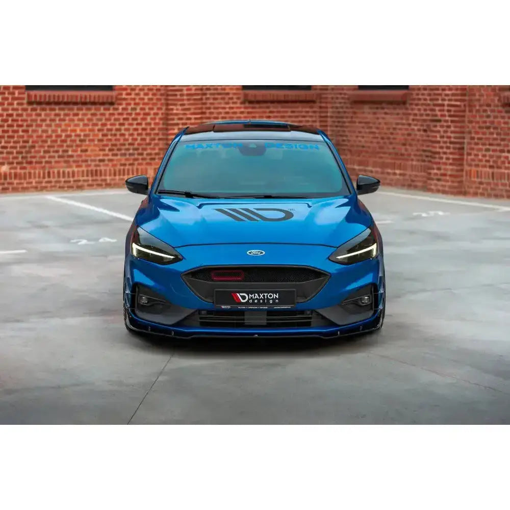 Frontleppe Ford Focus Mk4 St-Line på blå sportsbil med sort grill og striper, sett forfra mot mursteinsvegg.